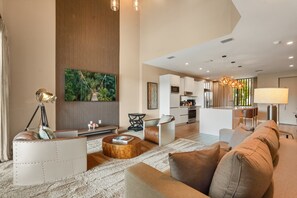 A spacious living area with a large sofa, a coffee table, and a seating area with a small table and chairs. There is a kitchen area visible in the background with modern appliances. - Pininfarina Masterpiece 4 BD/4.5 BA - 5534 PW (Kissimmee)