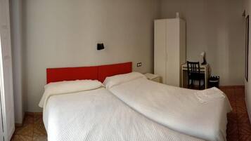 Una habitación con cama, armario, escritorio con silla y lámpara.