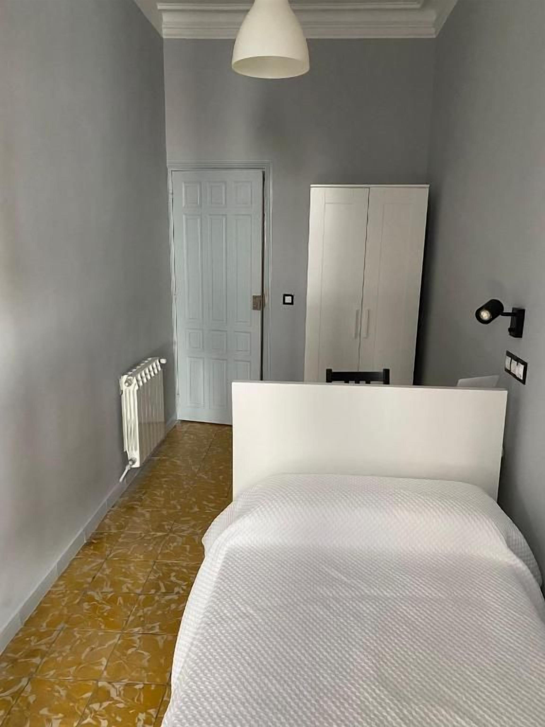 Un dormitorio con cama, armario, radiador y lámpara.