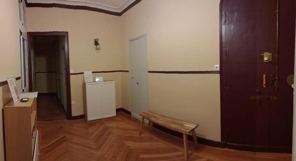 Un corridoio con pavimento in legno, una panca, un elettrodomestico bianco e una porta.