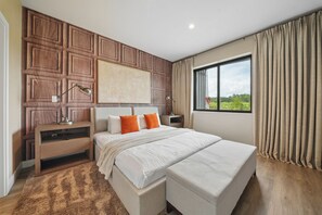 Ein Schlafzimmer mit einem großen Bett, einem Nachttisch, einer Lampe, einem Fenster mit Vorhängen und Blick ins Grüne.