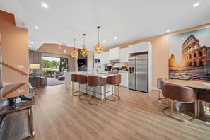 A modern kitchen with a central island, bar stools, and a large window. - Modern Oasis 4 BD/4.5 BA Magic Village by Pininfarina - 5501 TR (Kissimmee)
