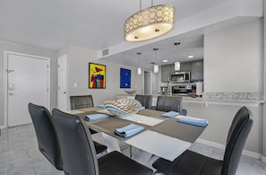 Un coin repas avec une table dressée pour quatre personnes, une cuisine en arrière-plan et des œuvres d’art accrochées aux murs.