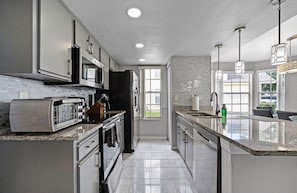 A modern kitchen with stainless steel appliances, a granite countertop, and a large window providing natural light. - 3 BD/ 2 BA/ The Villas at Laguna Bay (5017-95 LB) (Kissimmee)