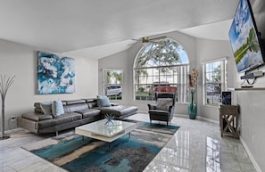 A spacious living room with a sectional sofa, a coffee table, and a large window offering a view of the outside. - 3 BD/ 2 BA/ The Villas at Laguna Bay (5017-95 LB) (Kissimmee)
