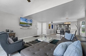 A modern living room with a flat-screen TV, a sofa, a coffee table, and a dining area in the background. - 3 BD/ 2 BA/ The Villas at Laguna Bay (5017-95 LB) (Kissimmee)