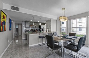 A modern kitchen with stainless steel appliances, a dining area with a glass table and black chairs, and a large window providing natural light. - 3 BD/ 2 BA/ The Villas at Laguna Bay (5017-95 LB) (Kissimmee)