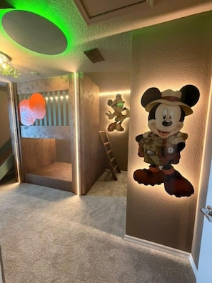 Een hal met een Mickey Mouse decoratie aan de muur, een houten ladder en een deur met een lamp.