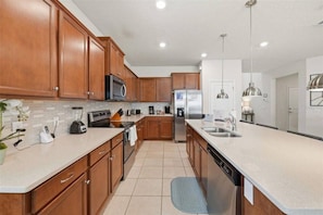 A modern kitchen with wooden cabinets, stainless steel appliances, and a large island with a sink. - 8 BD/ 6 BA/ Windsor Island - 2290 LC (Davenport)