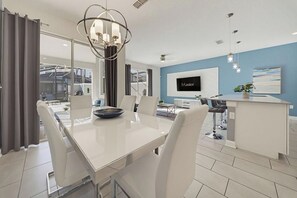A modern kitchen with a large island, a dining area with a glass table, and a TV mounted on the wall. - 4 BD/ 3 BA/ Storey Lake - 4816 ML (Kissimmee)