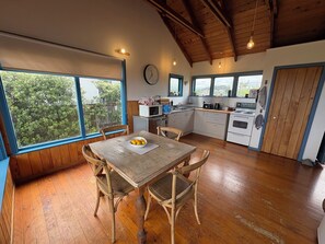 A kitchen with wooden flooring, a dining table with chairs, a microwave, and a stove. - Relax at our Beach Front Cosy 2 Bed Bach (Waitārere Beach)