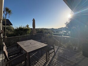 A wooden deck with a table and chairs, overlooking a residential area with houses and trees. - Relax at our Beach Front Cosy 2 Bed Bach (Waitārere Beach)