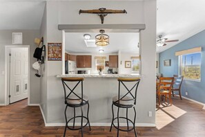 A kitchen with a bar area, wooden stools, and a ceiling fan. - Wild West Town and Ranch Casita; 7 min. from Arizona Athletic Grounds AAG (Mesa)