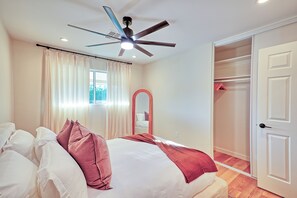 Une chambre à coucher comprenant un lit, un ventilateur de plafond, une fenêtre avec des rideaux, un miroir et un placard.