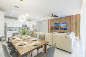 Un espace repas moderne avec une table en bois dressée pour quatre personnes, un canapé et un téléviseur fixé au mur.