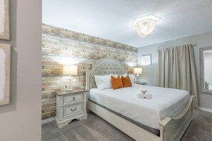 Une chambre à coucher comprenant un lit, des tables de chevet, un luminaire fixé au mur et une fenêtre avec des rideaux.