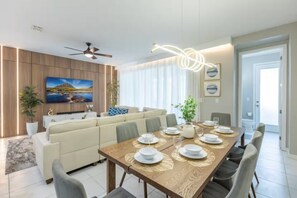 A modern dining area with a wooden table set for six, a sofa, and a ceiling fan. - Immersive 5 BD/ 4.5 BA/ Solara Resort - 1592 CP (Kissimmee)