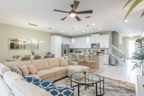 A modern living room with a sectional sofa, a glass coffee table, and a ceiling fan. - Immersive 5 BD/ 4.5 BA/ Solara Resort - 1592 CP (Kissimmee)