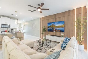 A modern living room with a sofa set, a coffee table, and a flat-screen TV mounted on a wooden wall. - Immersive 5 BD/ 4.5 BA/ Solara Resort - 1592 CP (Kissimmee)