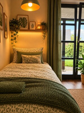A bedroom with a bed, a green throw blanket, a hanging lamp, and a view of the outdoors through a glass door. - New Listing (Welschneudorf)