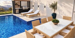 A poolside area with a dining table, lounge chairs, and a barbecue grill. - Enchanted 5 BD/ 4.5 BA/ Windsor Cay - 16262 CC (Clermont)
