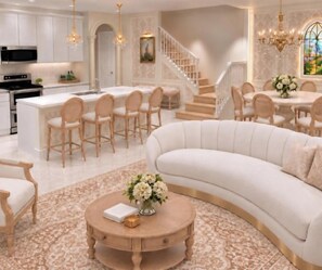 A spacious living area with a curved white sofa, a round coffee table with a vase of flowers, and a kitchen in the background. - Enchanted 5 BD/ 4.5 BA/ Windsor Cay - 16262 CC (Clermont)