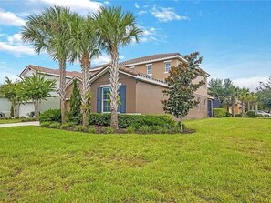A two-story house with a well-maintained lawn, palm trees, and a clear blue sky. - 6 BD/ 5.5 BA/ Solterra Resort - 5207 WW (Davenport)