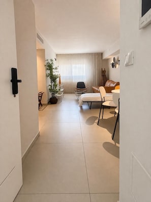 Ett modernt hotellrum med en säng, ett skrivbord, en stol, en krukväxt och ett stort fönster med gardiner.
