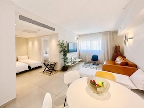 A modern hotel room with a bed, a seating area with a table and chairs, a television, and a window with curtains. - סוויטה מרווחת  וממוזגת מיקום מנצח 5דקות הליכה מהים במתחם בריכת שחייה 
sea said92 (Eilat)