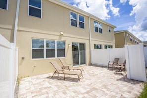 A two-story building with a patio area featuring outdoor furniture. - Cozy 4 BD/ 3.5 BA/ Compass Bay - 5149 AD (Kissimmee)