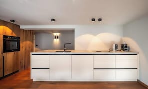 A modern kitchen with a central island, built-in oven, and a coffee machine. - WARM ALPINE CHARM MEETS MODERN COMFORT IN THIS CENTRAL RETREAT (Zermatt)