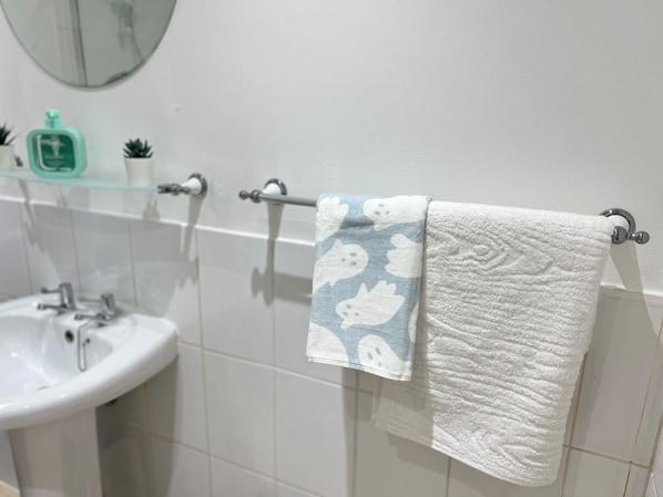 A bathroom with a white sink, a glass shelf with toiletries, and a towel rack with two towels. - Extra-Large Manchester City Centre Flat | 2 Bedrooms, 2 Bathrooms & TV Room (Manchester)