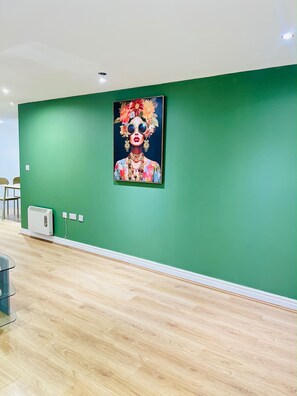 A room with a green wall, a framed artwork, a white air conditioning unit, and a wooden floor. - Extra-Large Manchester City Centre Flat | 2 Bedrooms, 2 Bathrooms & TV Room (Manchester)