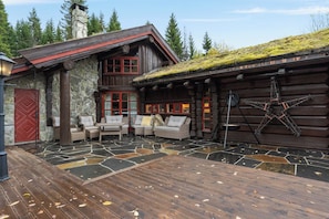 A log cabin with a stone exterior, a red door, and a wooden deck with outdoor furniture. - TH689 Log cabin by the Libakken lift, Sleeps 12 (Trysil)