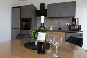 A bottle of wine on a table with two glasses, a potted plant, and a kitchen in the background. - Lity Apartment Green (Podglavica)