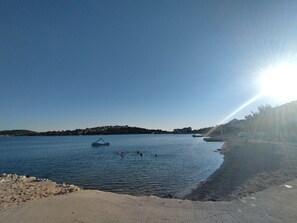 A beach with clear water, a boat, and a distant shoreline. - Lity Apartment Green (Podglavica)