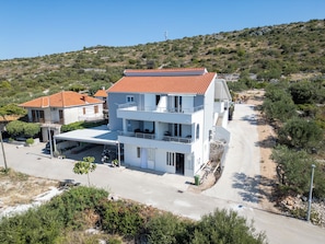 A multi-story building with a red-tiled roof, balconies, and a paved driveway. - Lity Apartment Green (Podglavica)