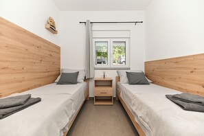 A bedroom with two beds, a window with a view, and a small bedside table. - Lity Apartment Green (Podglavica)