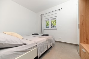 A small, modern bedroom with a single bed, a window with a view of trees, and a wooden wardrobe. - Lity Apartment Green (Podglavica)