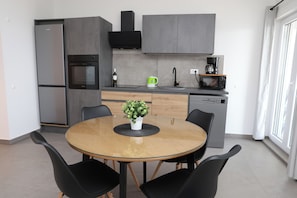A modern kitchen with a dining table, chairs, a coffee machine, and a wine bottle. - Lity Apartment Green (Podglavica)