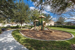 A playground with a slide and climbing structures surrounded by grass and trees. - Family Fun, 5BR with Pool, Games & Themed Rooms (Kissimmee)