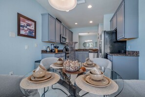 A modern kitchen with grey cabinets, a glass dining table, and a kitchen island. - Family Fun, 5BR with Pool, Games & Themed Rooms (Kissimmee)