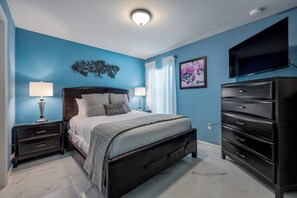 A bedroom with a bed, nightstands, a dresser, a television, and a ceiling light. - Family Fun, 5BR with Pool, Games & Themed Rooms (Kissimmee)