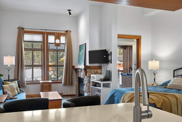 A hotel room with a bed, desk, chair, television, and a fireplace. - Ski-In/Out Luxury Village Studio! (Sun Peaks)