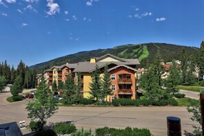 A multi-story hotel with balconies, surrounded by trees and a mountain backdrop. - Ski-In/Out Luxury Village Studio! (Sun Peaks)