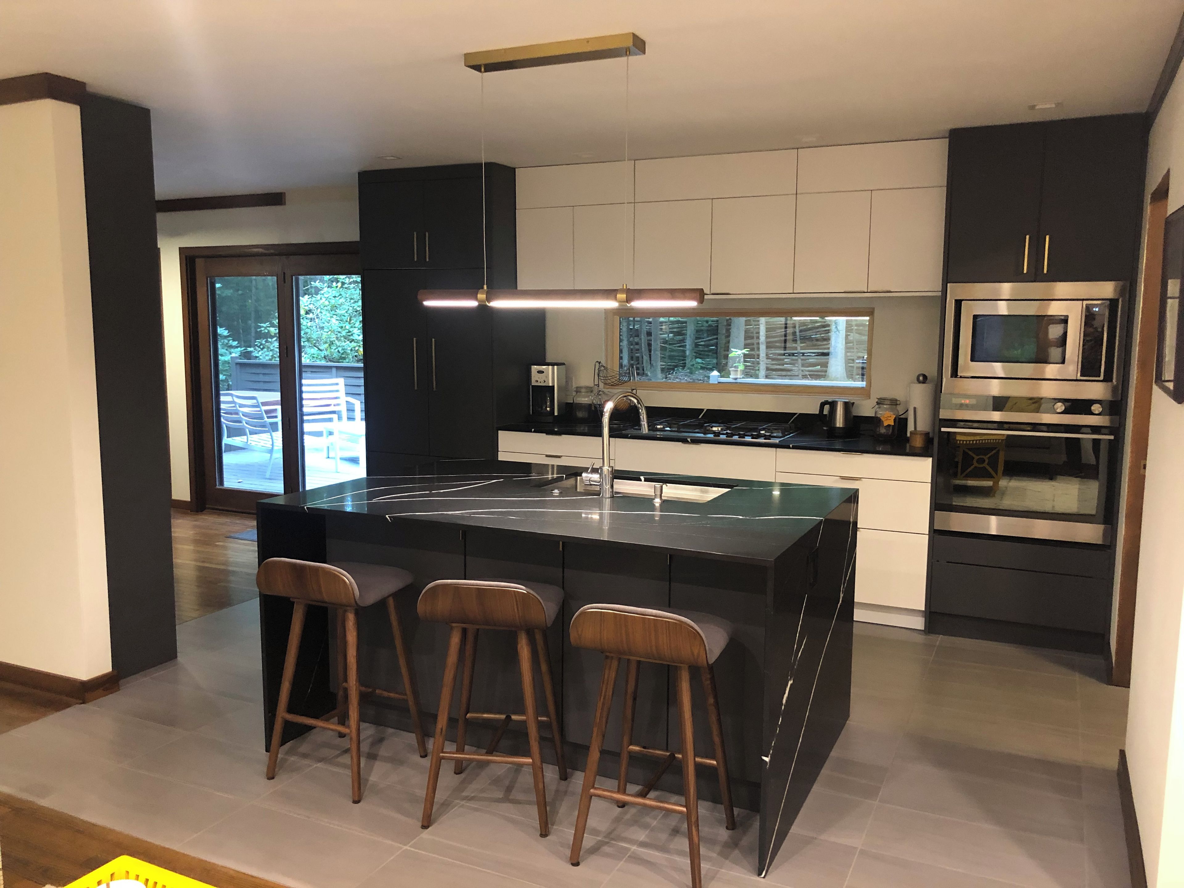 A modern kitchen with a central island, bar stools, a built-in oven, and a large window.