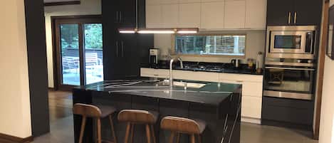 A modern kitchen with a central island, bar stools, a built-in oven, and a large window.