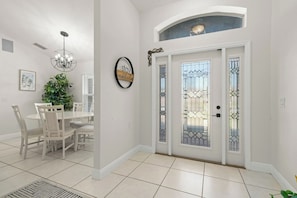 A dining area with a white table and chairs, a chandelier, and a potted plant. - The Perfect 3BR Villa | Beautiful Lanai and Luxury (Cape Coral)