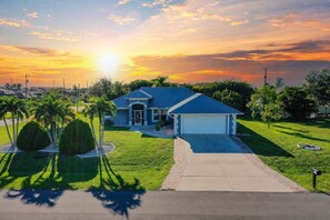 A residential house with a blue roof, a front driveway, and a well-maintained lawn with palm trees. - The Perfect 3BR Villa | Beautiful Lanai and Luxury (Cape Coral)