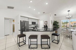 A modern kitchen with a central island, bar stools, and a dining area with a view. - The Perfect 3BR Villa | Beautiful Lanai and Luxury (Cape Coral)